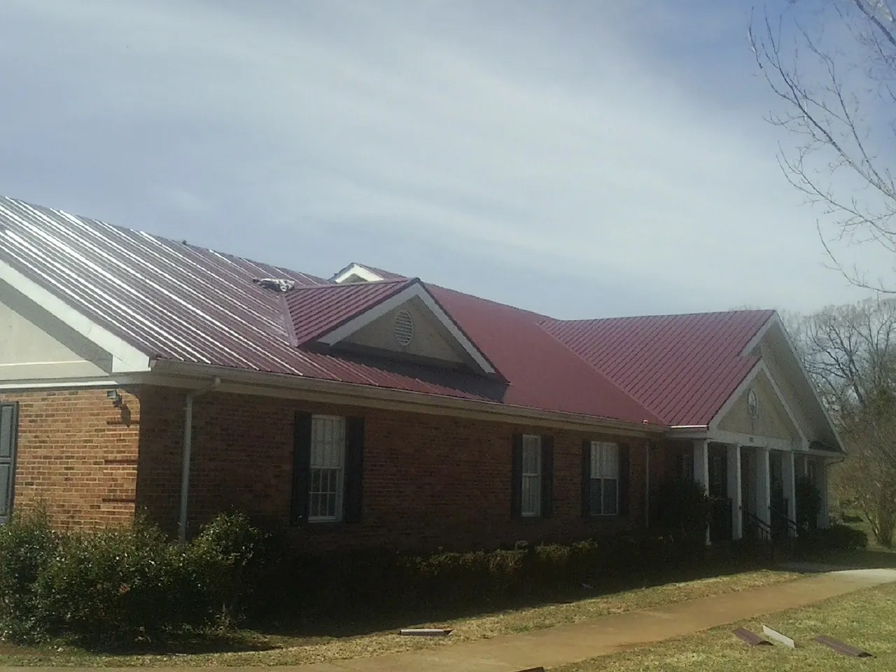 Red metal roof with gabled entries on a long brick building, from a Hail Damage Roof Repair job in Harris