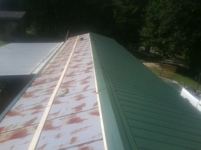Old rusted panels beside newly installed green metal roofing — Wind Damage Roof Repair by Roofing Brothers in Harris