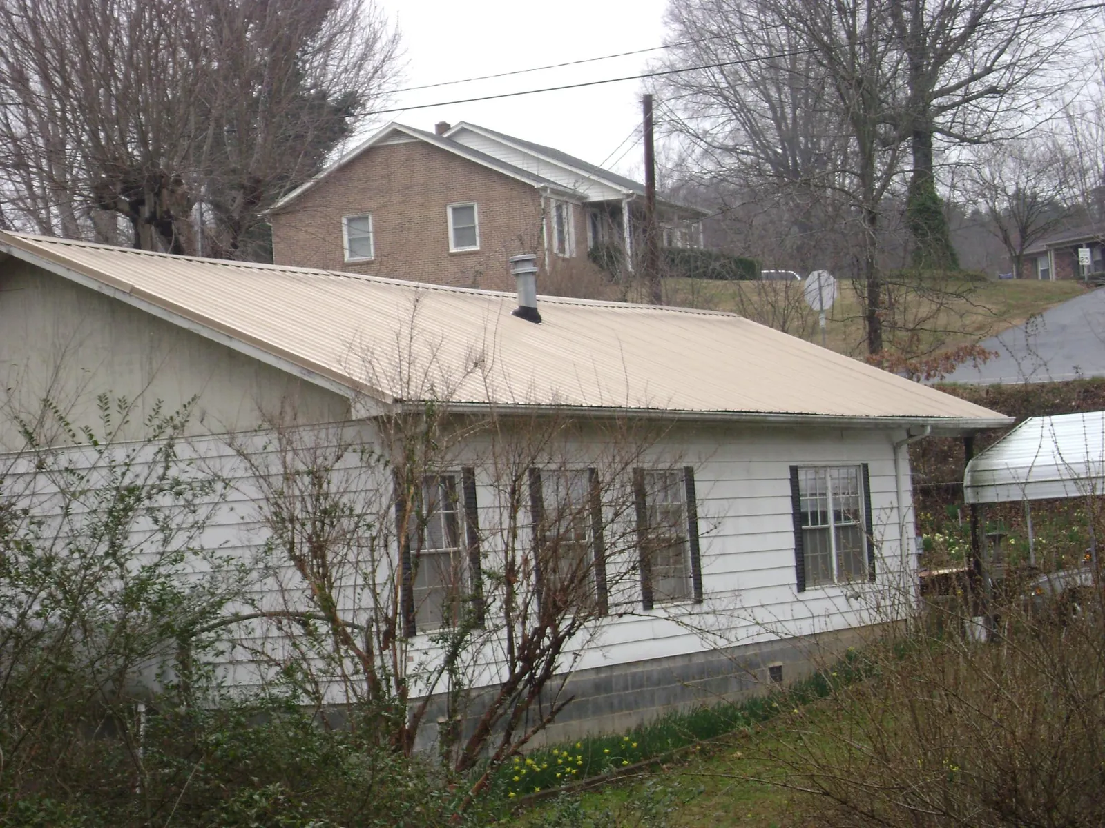 Tan metal roof on a white sided house set into a hillside — Commercial Roofing by Roofing Brothers in Harris
