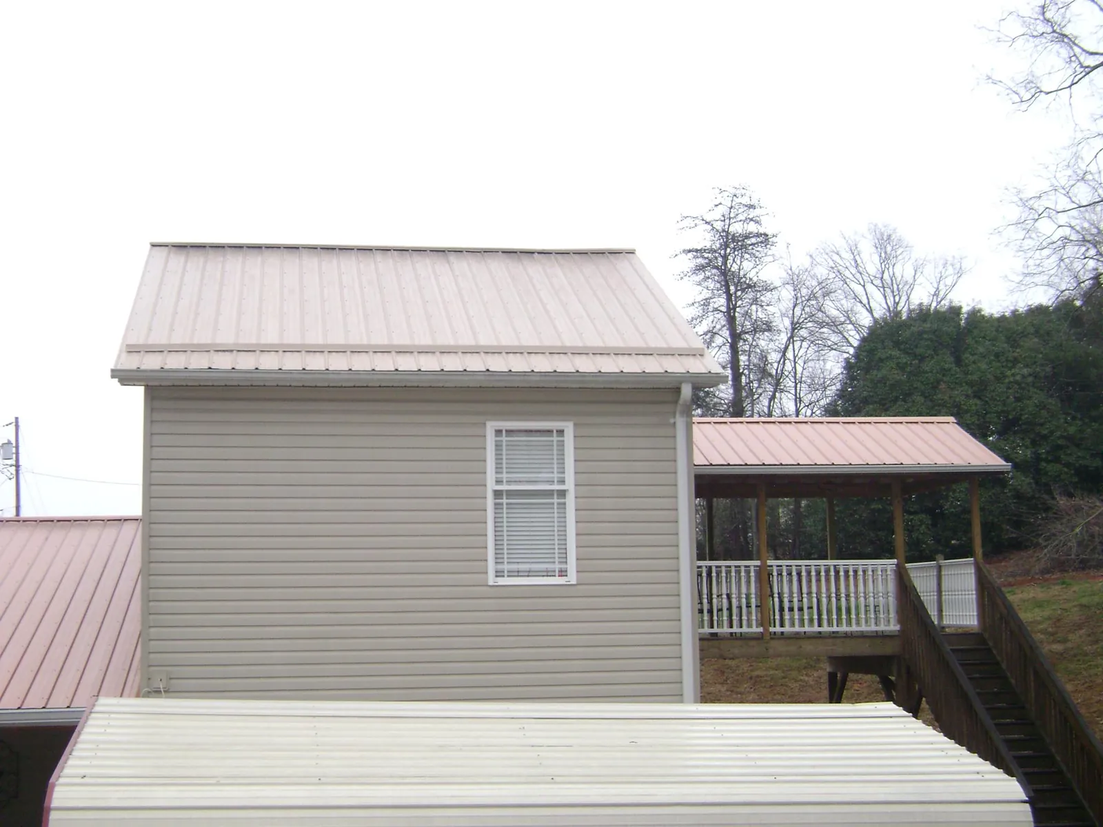 Tan metal roofs on a two story addition and attached porch, from a Roof Replacement job in Harris